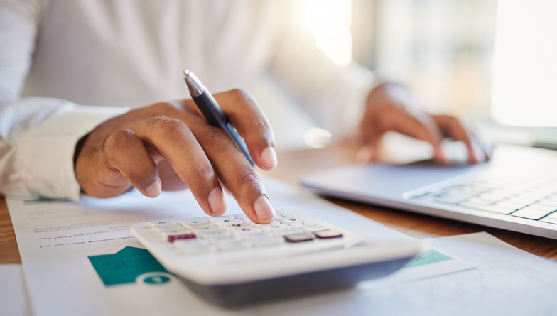 Close-up of a person’s hands using a calculator and laptop while reviewing financial documents, symbolizing smart budgeting and financing for home renovation projects.