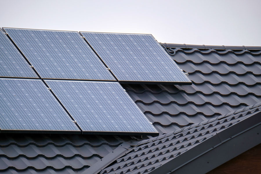 Detailed view of sleek black solar panels mounted on a dark gray tiled roof, showcasing clean installation lines and energy-efficient design against a muted sky.
