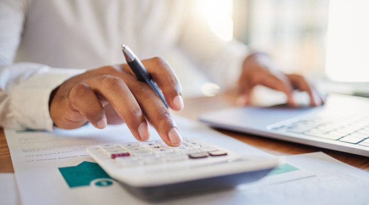 Close-up of a person’s hands using a calculator and laptop while reviewing financial documents, symbolizing smart budgeting and financing for home renovation projects.