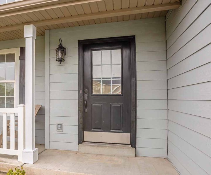 Welcoming front entrance with light gray horizontal siding, black paneled front door with glass insert, white porch columns, and vintage-style lantern lighting.